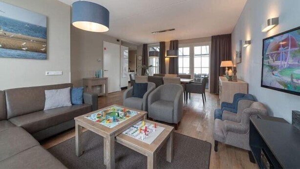 Un salon moderne comprenant un canapé, des fauteuils, une table basse et un coin repas avec une lampe.