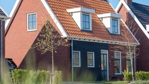 Une maison à deux étages, avec un toit recouvert de tuiles rouges, des encadrements de fenêtres blancs et une façade bleu foncé.