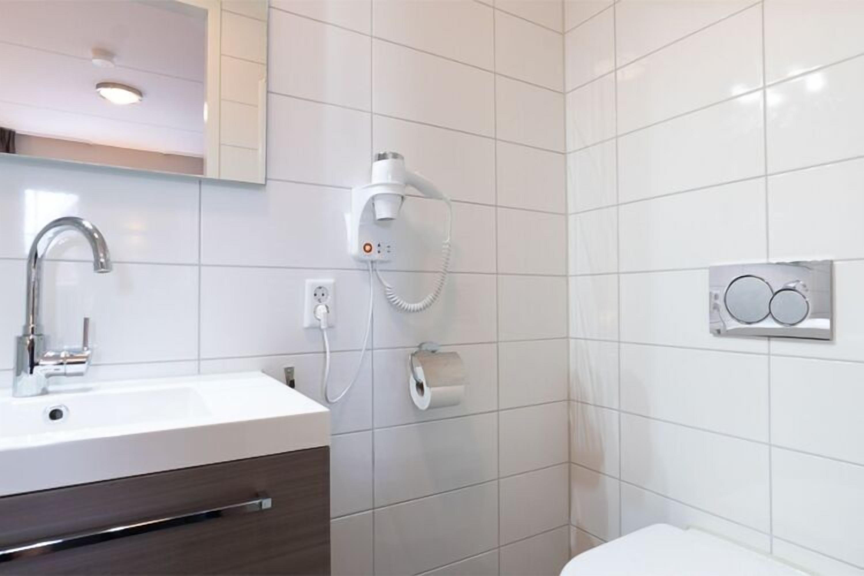 Ein modernes Badezimmer mit einem weißen Waschbecken, einem Spiegel, einem Fön und einer Toilette.