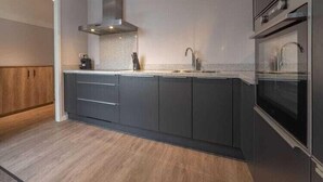 Une cuisine moderne avec des meubles de couleur sombre, une hotte en acier inoxydable, un évier à deux bacs et un four encastré.