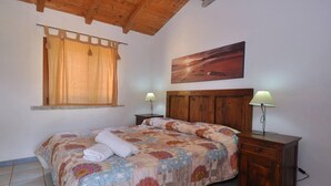 Una camera da letto con un letto in legno, una finestra con tende, un comodino con una lampada e un quadro appeso al muro.