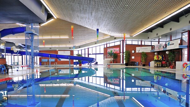 En indendørs swimmingpool med blå og hvide farver, et blåt spiralrutsjebane og et træloft.