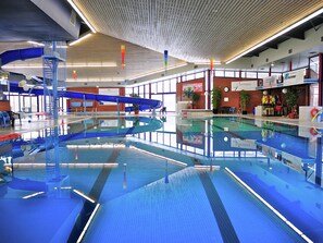 Een binnenzwembad met een blauw-wit kleurenschema, een blauwe spiraalglijbaan en een houten plafond.