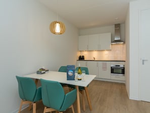A compact kitchen with white cabinets, a built-in oven, and a hanging pendant light. - Apartment in Zoutelande Near Sunny Beach (Zoutelande)