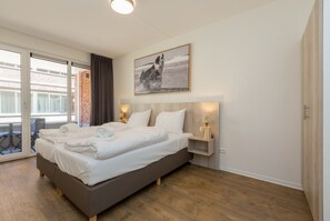 A modern hotel room with a large bed, a small bedside table, a wall-mounted picture, and a sliding glass door leading to an outdoor area. - Apartment in Zoutelande Near Sunny Beach (Zoutelande)
