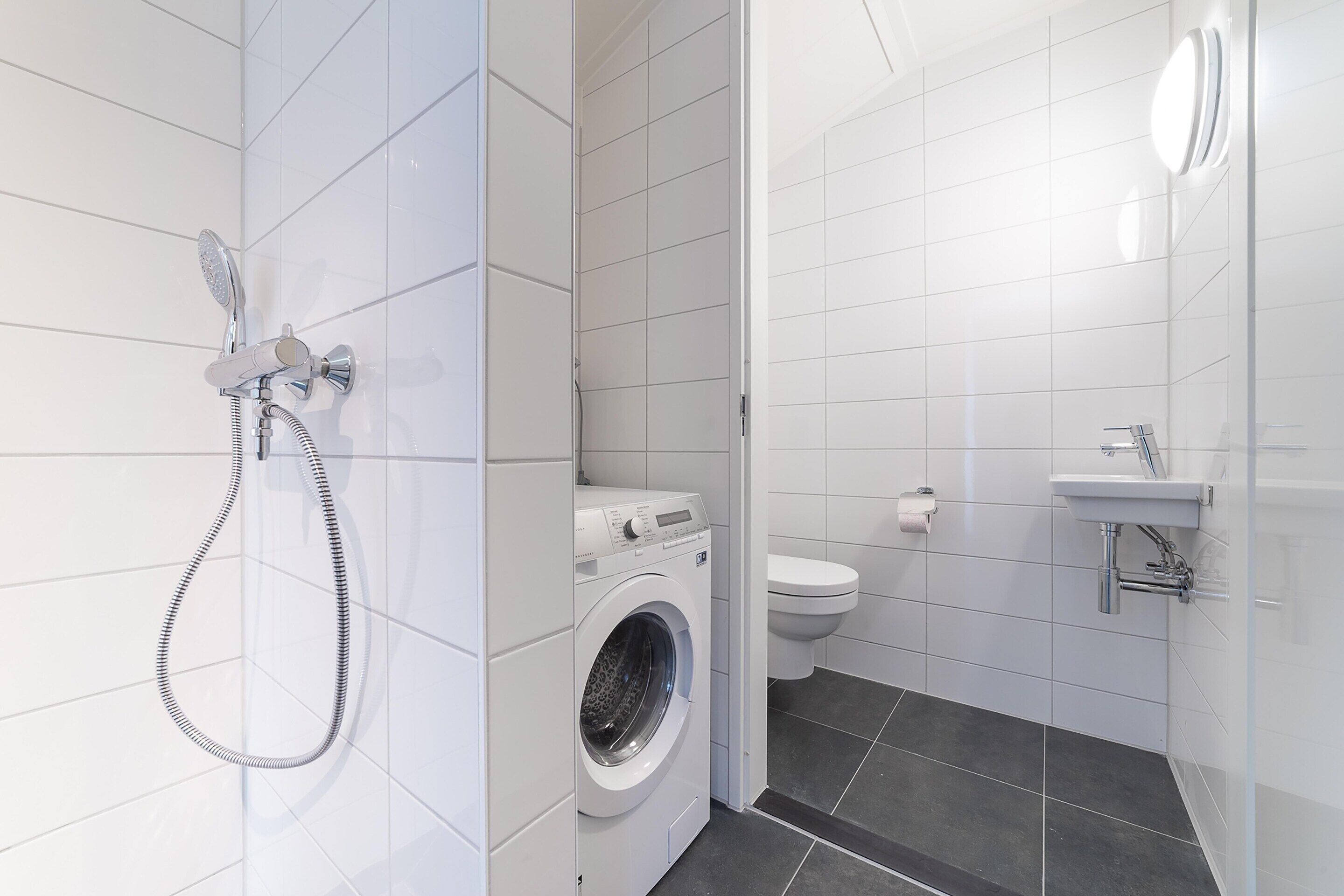 A modern bathroom with a washing machine, toilet, and sink.