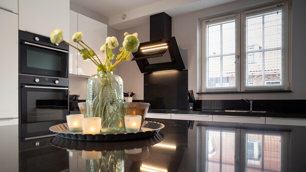 A modern kitchen with a black countertop, a vase with flowers, and candles.