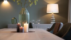 A dining table with candles, a vase with flowers, and a lamp with stacked stones.