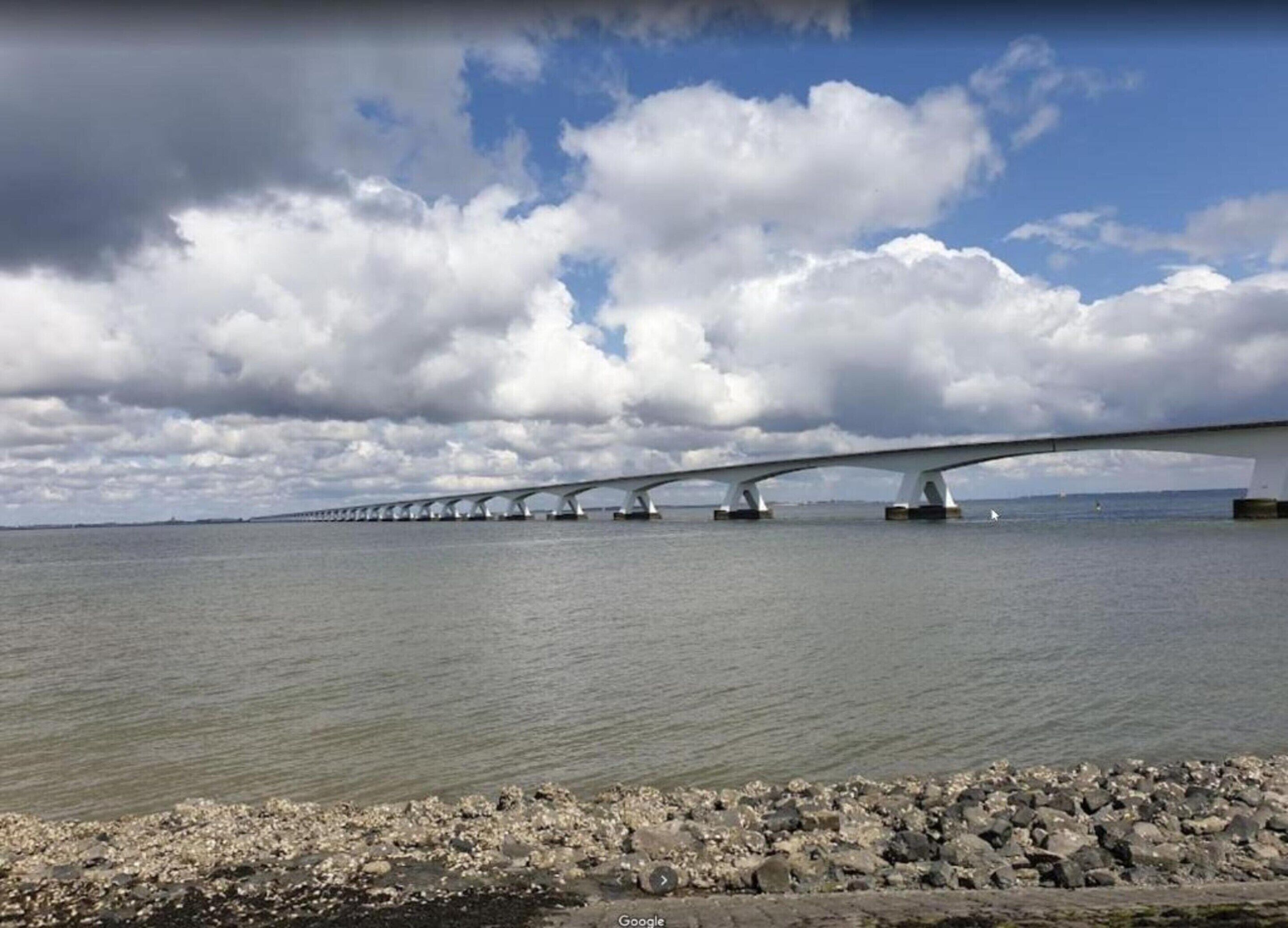 A long bridge with multiple arches over a body of water, with a rocky shoreline in the foreground.
