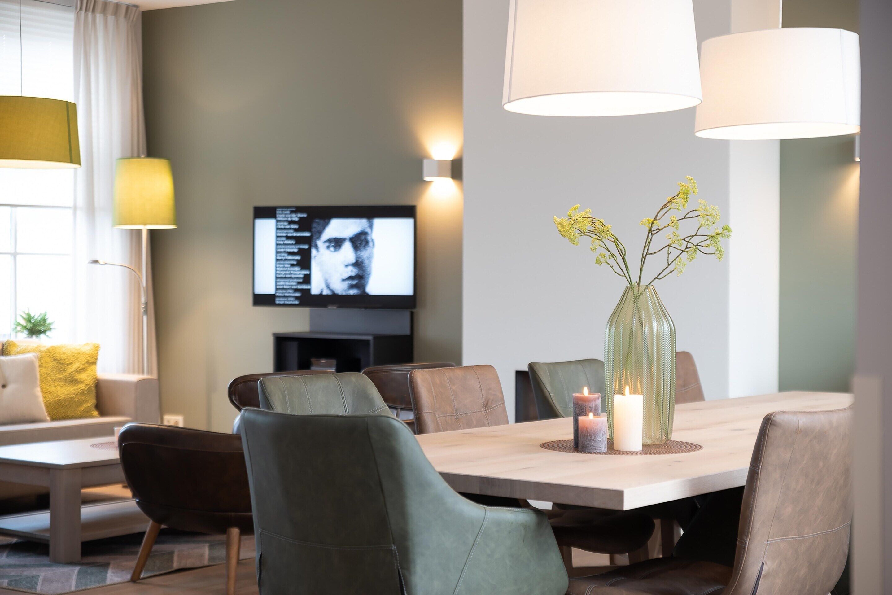 Un salon moderne avec une table à manger, des fauteuils en cuir, un téléviseur et un vase rempli de fleurs.