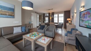 A modern living room with a sofa, armchairs, a coffee table with board games, a TV, and artwork on the walls.