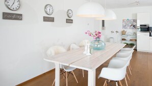 Eine moderne Küche mit weißen Schränken, einem eingebauten Backofen und einem Essbereich mit einem Holztisch und weißen Stühlen.