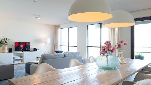 Ein modernes Wohnzimmer mit einem Holzesstisch, einem grauen Sofa und einem Fernseher an der Wand.
