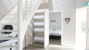 Habitació d'hotel moderna amb escala, llit, radiador i porta amb senyal d'emergència.