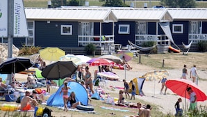 Una platja amb diverses tendes i ombrel·les, una filera de cases de platja al fons, i gent relaxant-se a la sorra.