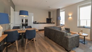 Una sala de estar moderna con un sofá, una mesa de comedor con sillas y una zona de cocina al fondo.
