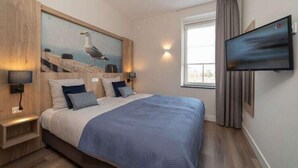 Un dormitorio con una cama, un cuadro de una gaviota, un televisor y una ventana con cortinas.