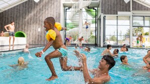 Una piscina amb diverses persones, incloent infants jugant i adults nedant.
