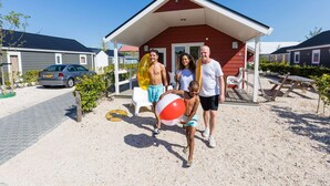 Una família amb un nen que sosté una pilota de platja davant d'una casa vermella amb un porxo.