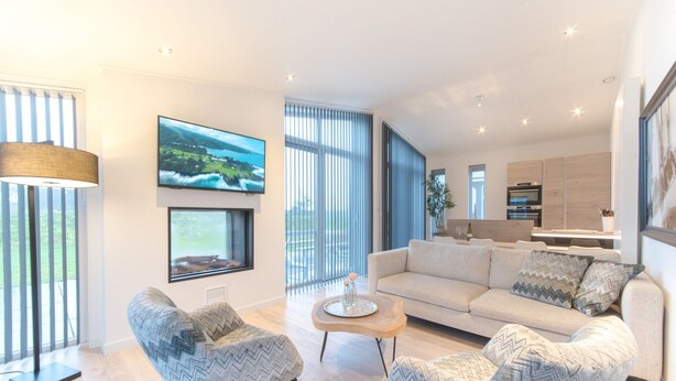 A modern living room with a sofa, two armchairs, a coffee table, and a TV mounted on the wall. - Cozy Chalet with Fireplace near Oosterschelde (Wemeldinge)