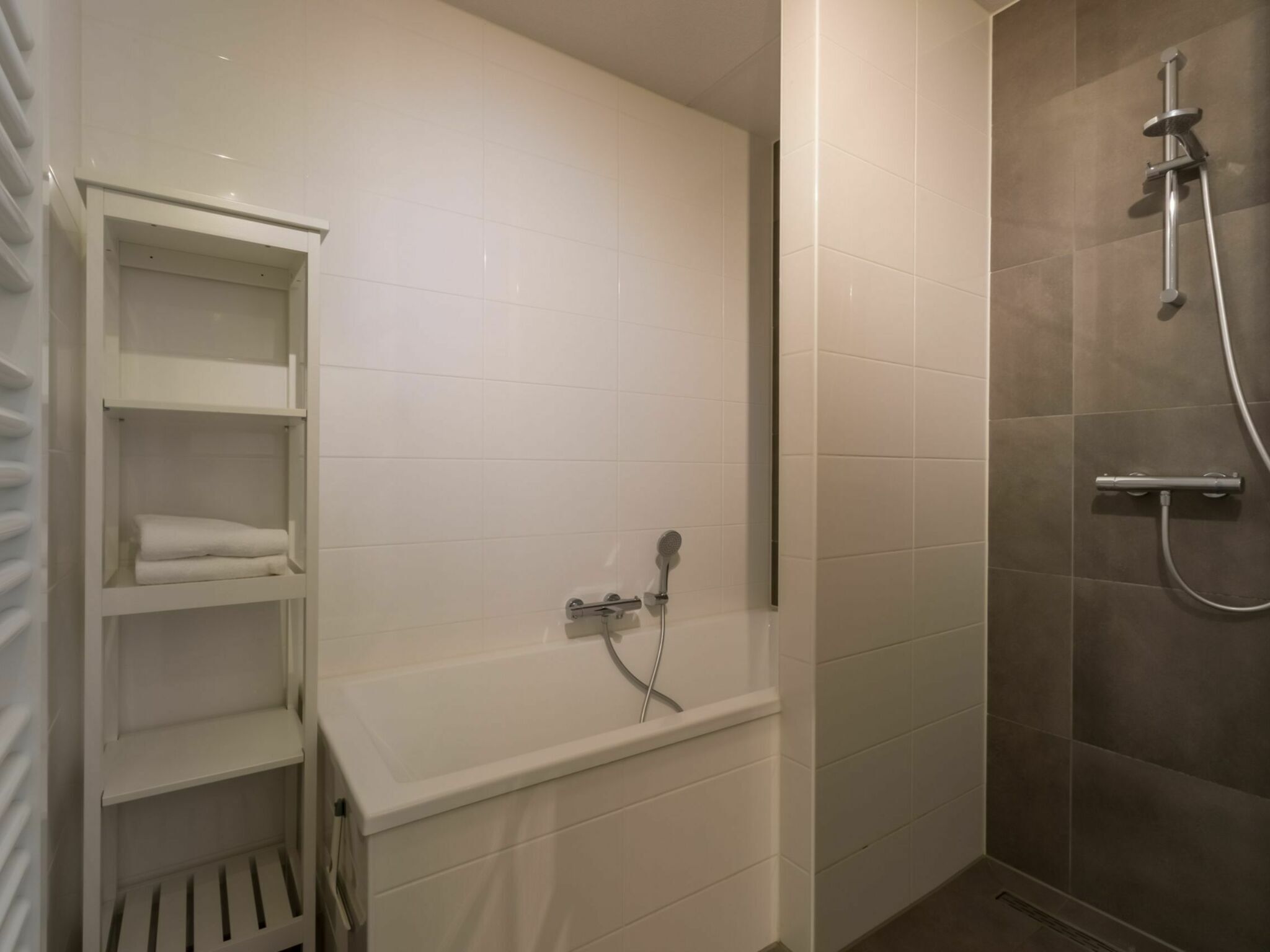 A bathroom with a shower, a white bathtub, and a shelf with towels.