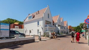 Een wit gebouw met een rode pannendak, een bord met tekst en een geplaveid pad.