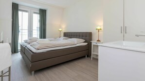 Een moderne hotelkamer met een groot bed, een nachtkastje, een lamp, een badkamer met een wastafel en een garderobe.