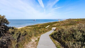 A coastal pathway leading to a lighthouse, with a clear sky and calm sea. - Apartment Near South Beach With Sauna (Koudekerke)
