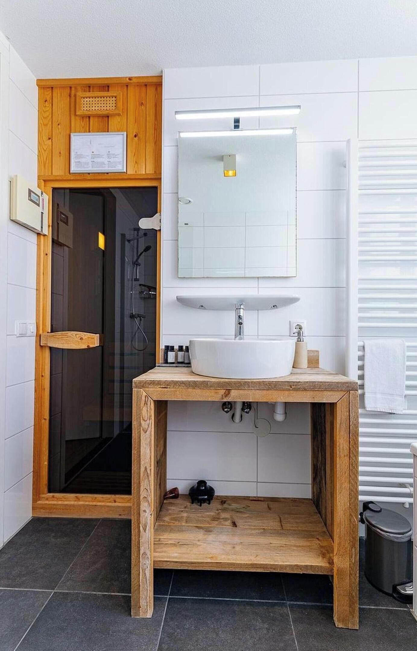 Een badkamer met een houten wastafelmeubel, een witte wasbak, een spiegel en een douchecabine.