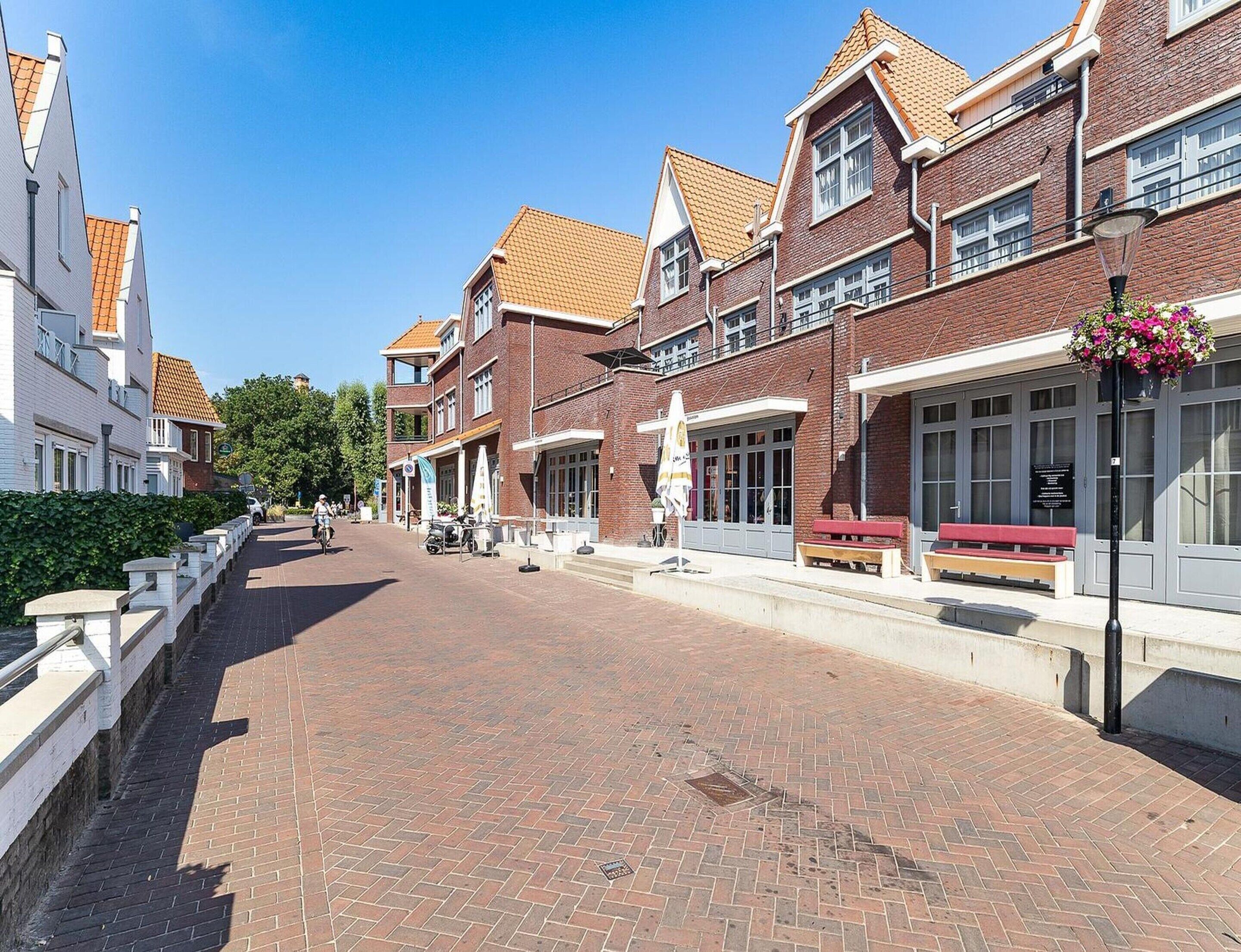Une rue pavée de briques, bordée de bâtiments des deux côtés, avec des bancs et un ciel dégagé.