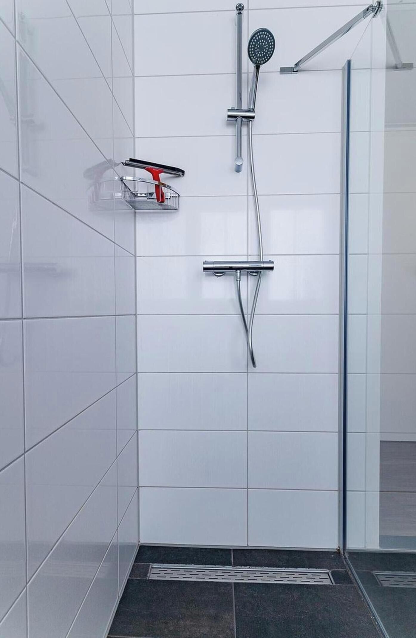 A shower with a handheld showerhead and a handheld sprayer, mounted on a wall with white tiles.
