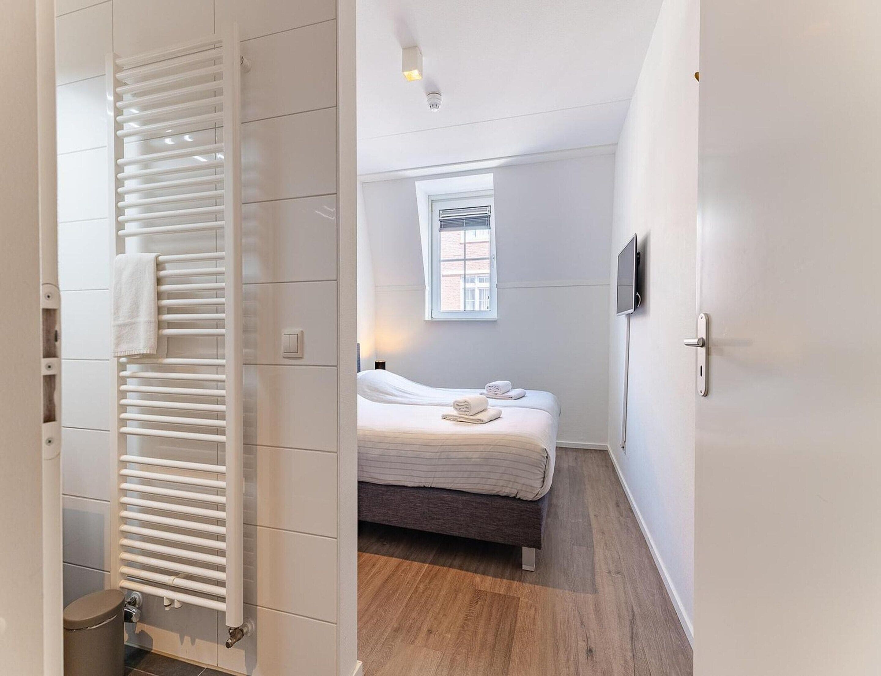 A hotel room with a bed, a window, a wall-mounted TV, and a radiator.