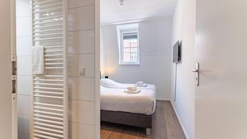 A hotel room with a bed, a window, a wall-mounted TV, and a radiator.