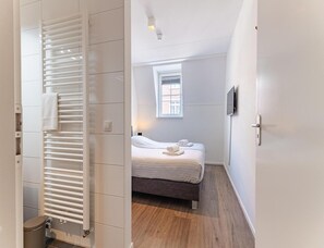 A hotel room with a bed, a window, a wall-mounted TV, and a radiator. - Apartment Near South Beach With Sauna (Koudekerke)