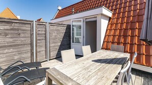 A wooden deck with a table and chairs, a sliding glass door, and a red-tiled roof. - Apartment Near South Beach With Sauna (Koudekerke)