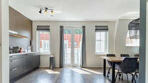 A modern kitchen with a dining area, large windows, and a view of the outside. - Apartment Near South Beach With Sauna (Koudekerke)
