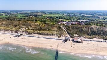 An aerial view of a coastal area with a beach, a pier, and a residential area with houses.