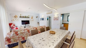 Ein modernes Wohnzimmer mit Fernseher, Sofa, Esstisch und Küchenzeile.