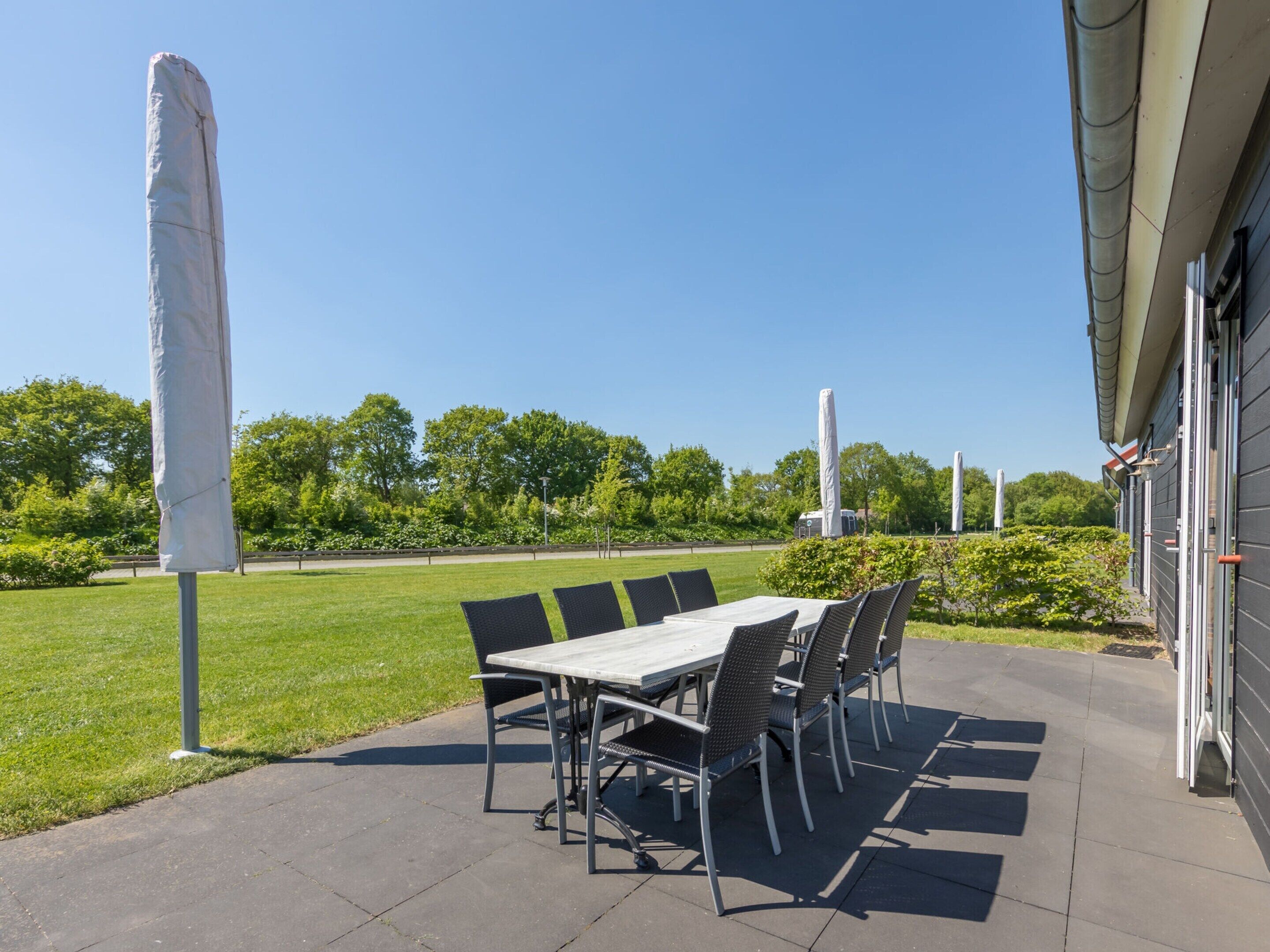 Une terrasse extérieure avec une table et des chaises, un parasol et un bâtiment en arrière-plan.