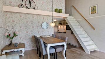 A dining area with a wooden table and chairs, a clock on the wall, and a staircase leading to an upper level.