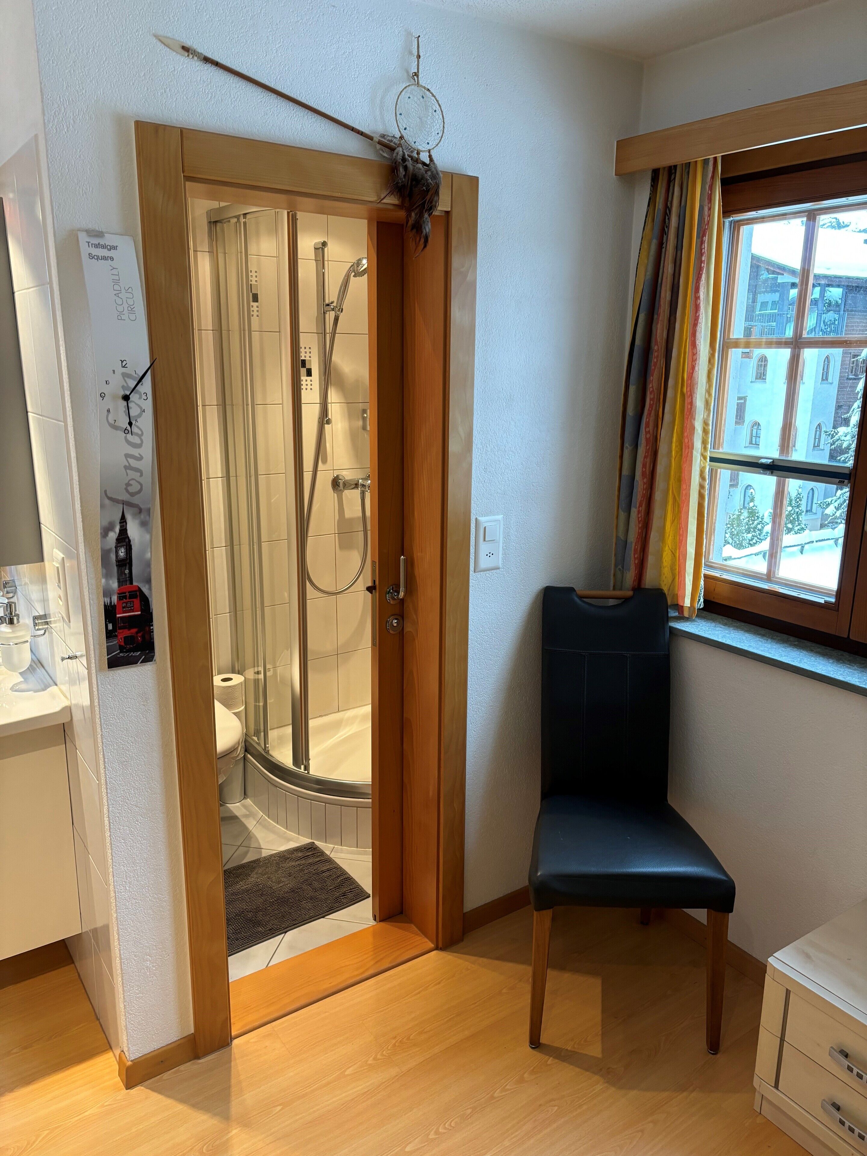 Ein Badezimmer mit Dusche, Toilette und einem Stuhl in der Nähe eines Fensters mit Blick auf Gebäude.