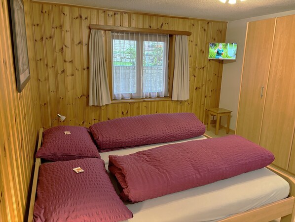 Ein Zimmer mit Holzvertäfelung, einem Bett mit zwei roten Kissen, einem kleinen Tisch und einem Fernseher an der Wand.