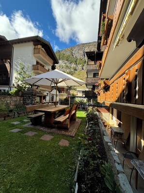 Ein Innenhof mit einem Holztisch und Bänken, umgeben von Steinmauern und Blick auf einen Berg.