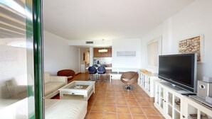 A modern living room with a sofa, a TV, and a dining area with chairs and a table. - ORQUIDEA LES OLIVERES (El Perelló)