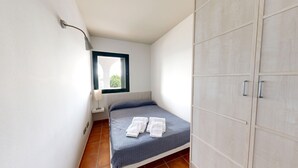 A small bedroom with a bed, a window, a lamp, and a wardrobe. - ORQUIDEA LES OLIVERES (El Perelló)