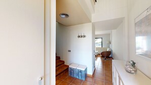 A hallway with a staircase, a white sofa, a wicker chair, and a small table with a decorative item. - ORQUIDEA LES OLIVERES (El Perelló)
