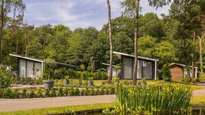 Un espacio exterior moderno con un estanque, plantas en macetas y varios edificios contemporáneos con grandes ventanales.