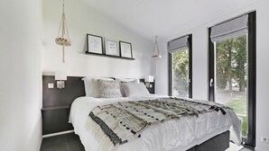 Un dormitorio moderno con una cama grande, una mesita de noche, una lámpara colgante y vistas al exterior.