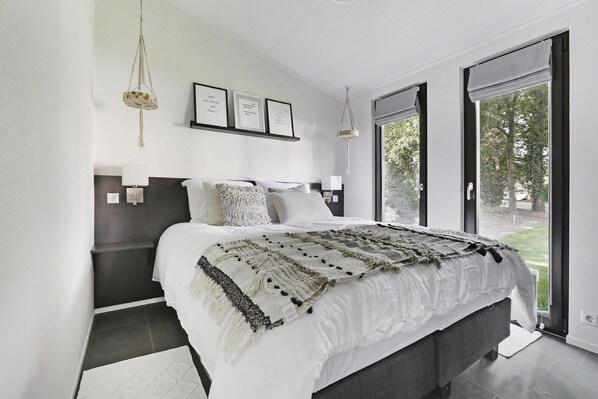 Un dormitorio moderno con una cama grande, una mesita de noche, una lámpara colgante y vistas al exterior.