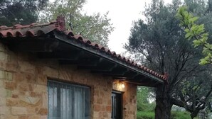 A rustic stone house with a tiled roof, a wooden bench, and a table outside.
